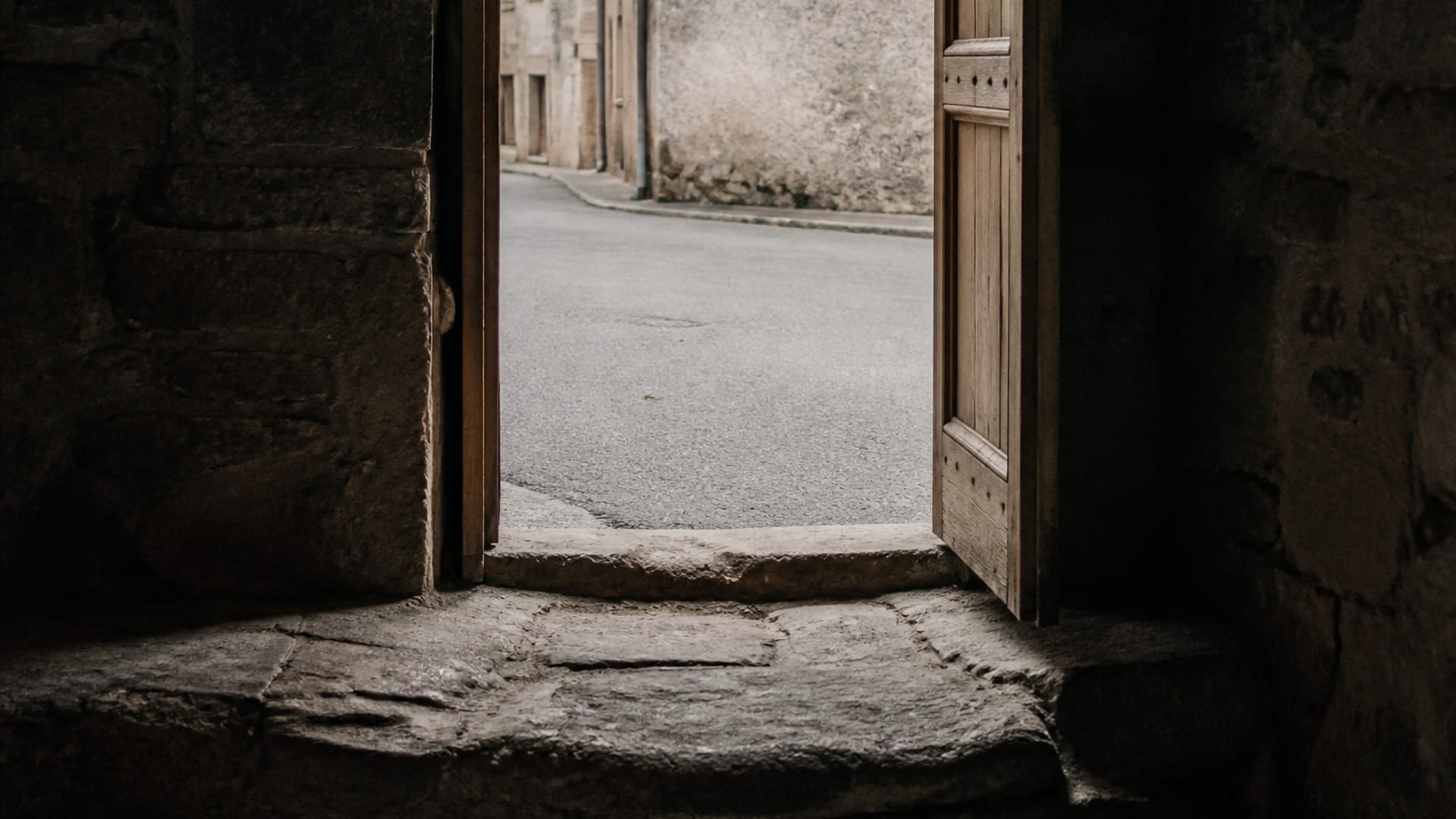A view from inside a dim stone room through an open doorway onto a bright ordinary street.