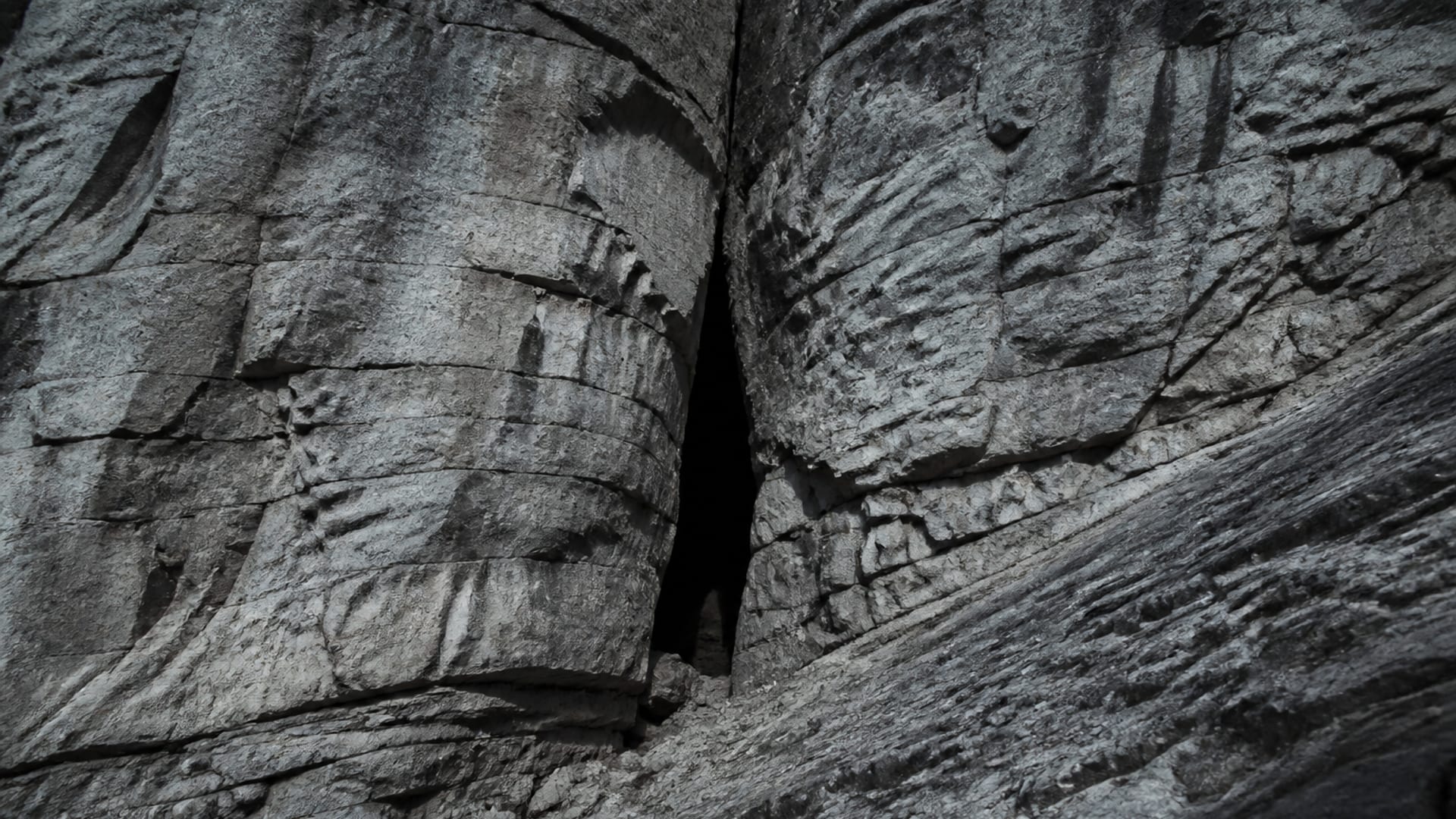A narrow cleft in a wind-scoured rock face on a bare mountainside.