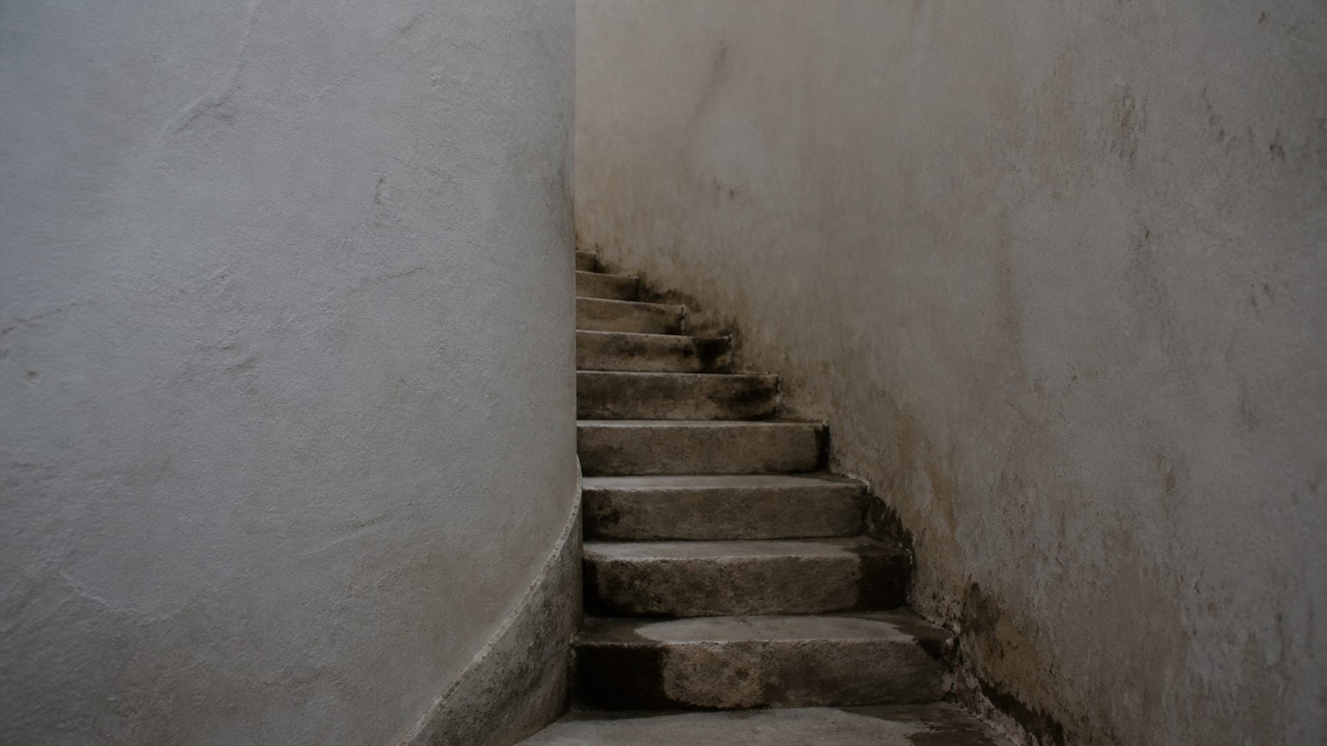 Worn stone steps turning a blind corner between two high plastered walls.